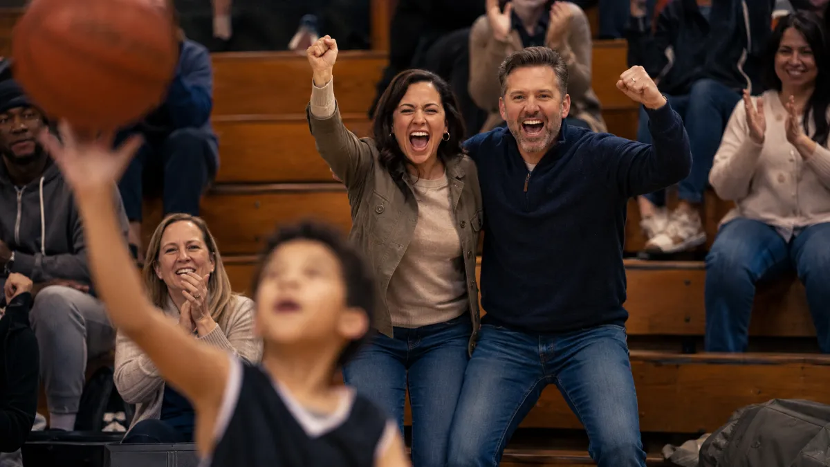 Two parents cheering together at their kid's basketball game